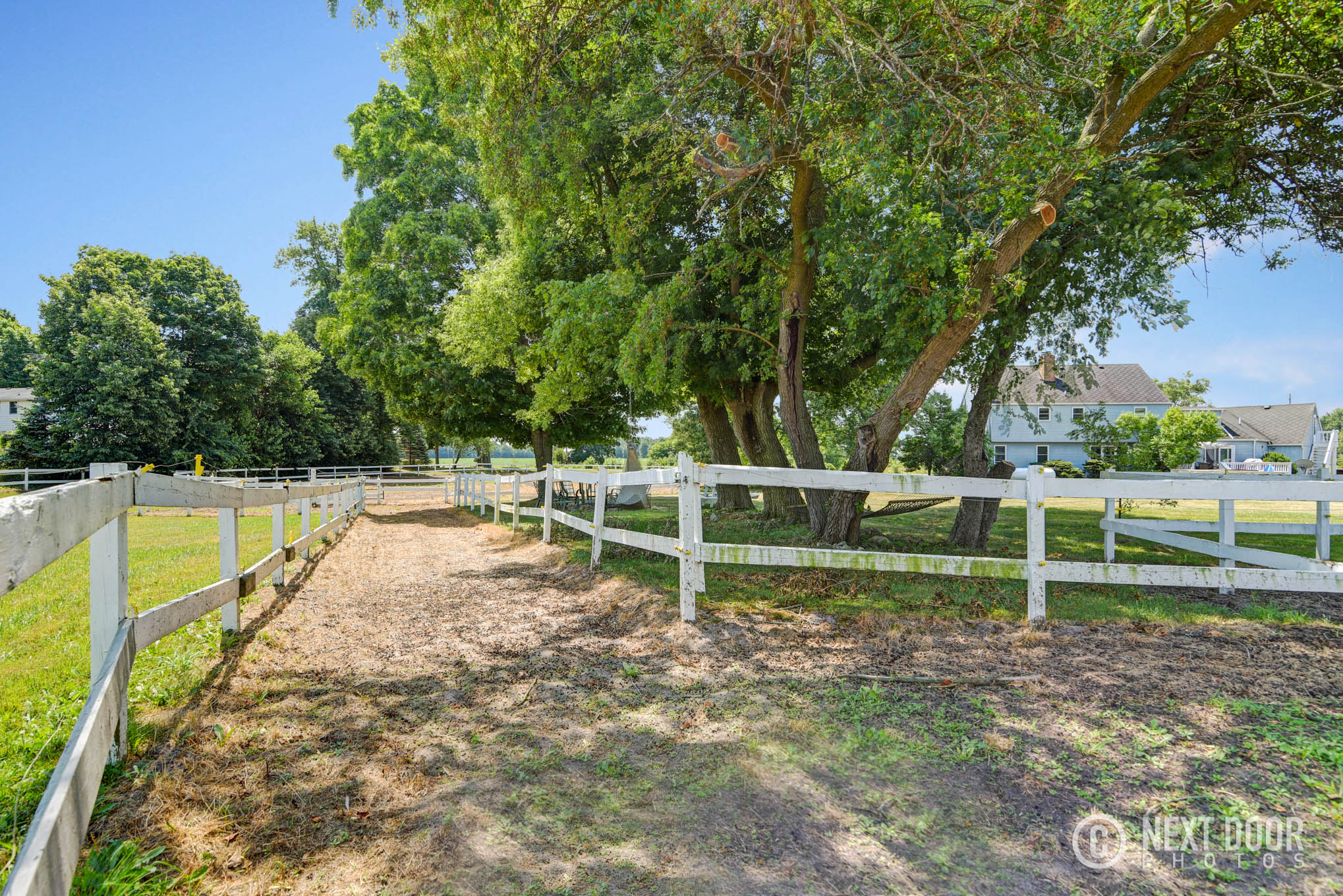 Fenced lanes, mature trees, and residence at a Lansing horse boarding property